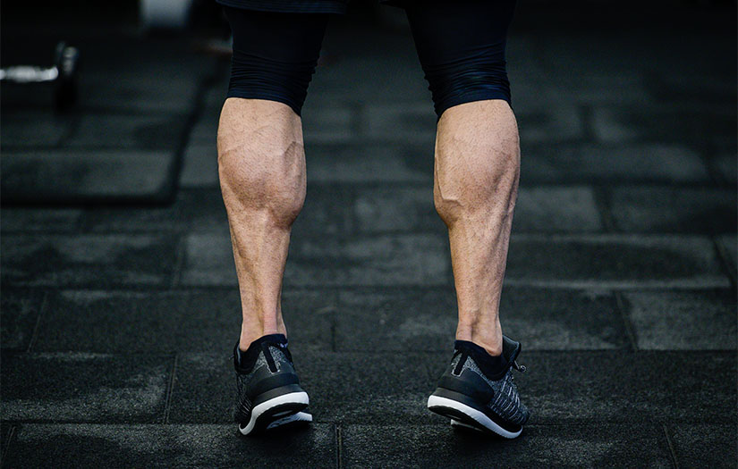 trained legs with muscular calves in sneakers in training gym during hard fitness and gym workout