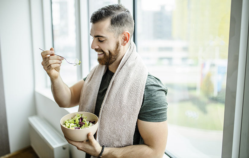 Young man eating fresh salad after intensive home workout